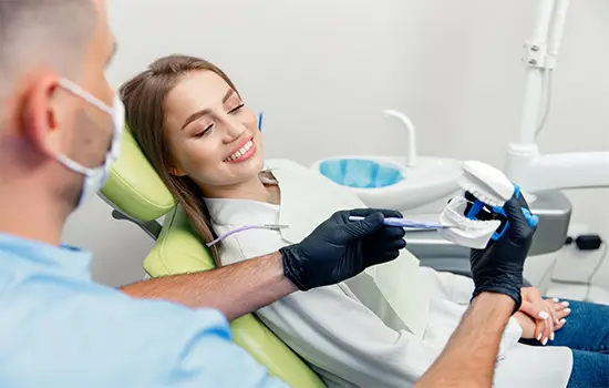 A dentist demonstrating dental care techniques to a smiling patient in a dental clinic.
